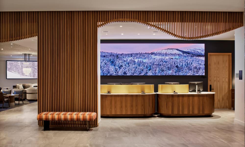 Modern reception desks with warm wood finishes and a panoramic mountain display above the front desk.