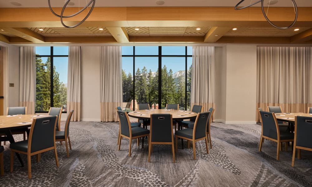 Modern conference and event space with round tables, upholstered chairs, and large windows overlooking the mountains.