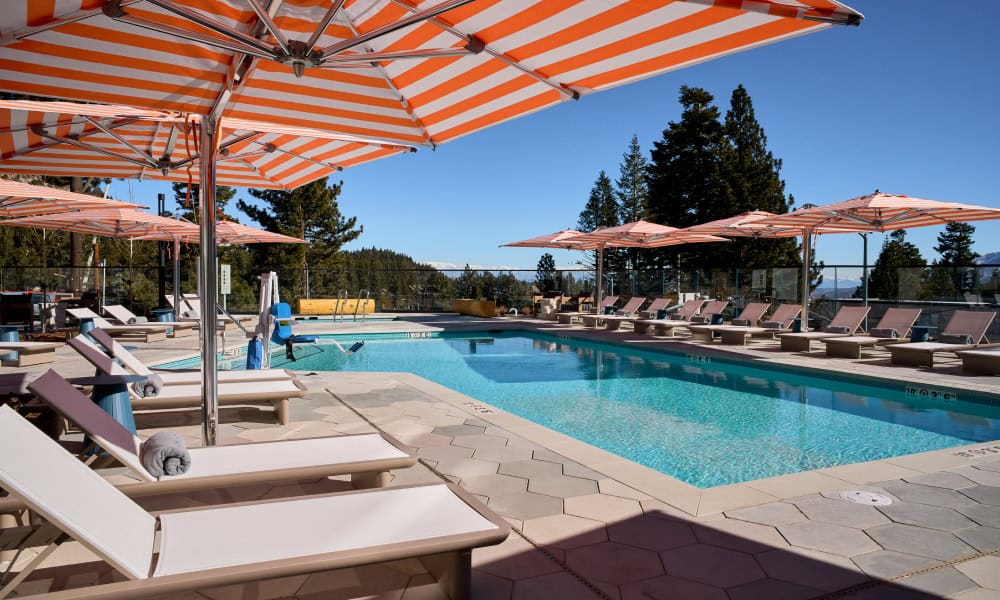Outdoor swimming pool surrounded by lounge chairs, orange-striped umbrellas, and mountain scenery.