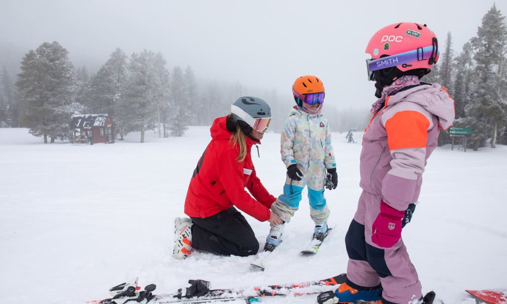 Skier in an orange jacket carving through deep powder snow on a mountain slope.