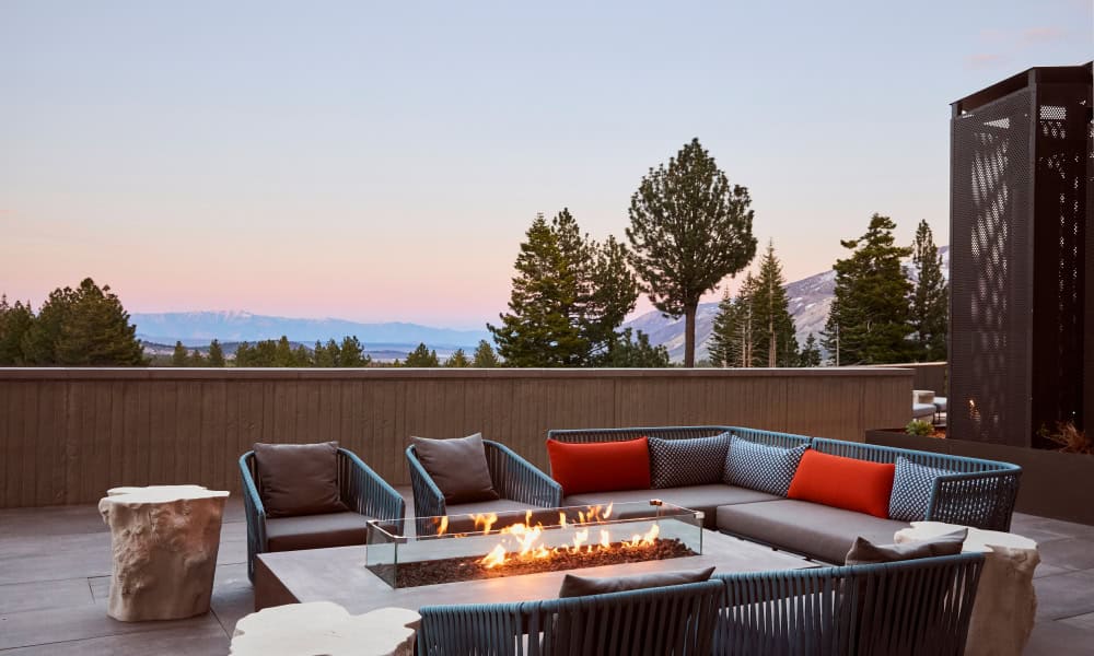 Outdoor terrace with cushioned lounge seating surrounding a fire pit overlooking the mountains at sunset.